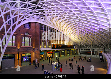 Menschen in der Nacht Innenraum des Kings Cross Eisenbahn-Zug Bahnhofsgebäude unter der modernen geschwungenen beleuchteten Dachkonstruktion Camden London England GB Stockfoto
