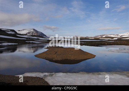 Noch teilweise gefroren Schmelzwasser Pool und den Berg Bjolfur im Bereich von Fjardarheidi in der Nähe von Seydisfjordur, Ost-Island Stockfoto