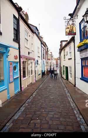 Whitby Town, North Yorkshire, UK, England schmale gepflasterte Straße mit Geschäften und Touristen zu Fuß die Straße runter Stockfoto