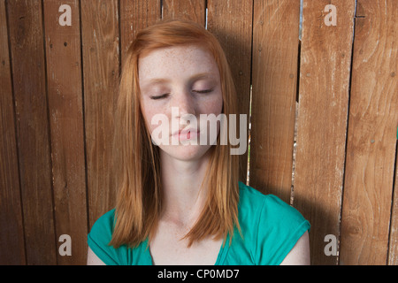 16 Jahre altes Mädchen mit roten Haaren sitzt im Freien mit geschlossenen Augen. Stockfoto