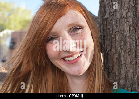 Porträt von lächelnden fünfzehn Jahre altes Mädchen mit roten Haaren neben einem Baum. Stockfoto