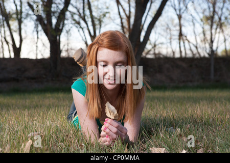 Ziemlich fünfzehn Jahre altes Mädchen mit roten Haaren hält Blatt in einem Feld Stockfoto