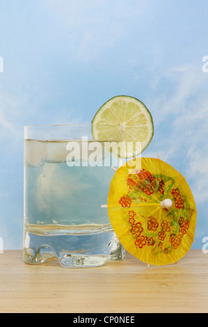 Kühlen und erfrischenden Limetten aromatisiert Getränke mit einer Scheibe Limette und einen cocktail Sonnenschirm vor blauem Himmel Stockfoto