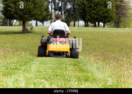 Ältere zog sich männliche schneiden das Gras oder mähen Rasen auf einem großen Rasen mit Gelb 0-turn Mäher Stockfoto