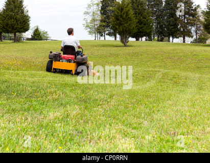 Senior im Ruhestand männlich mäht den Rasen auf weitläufigen Rasen mit gelben Zero-Turn Mäher Stockfoto