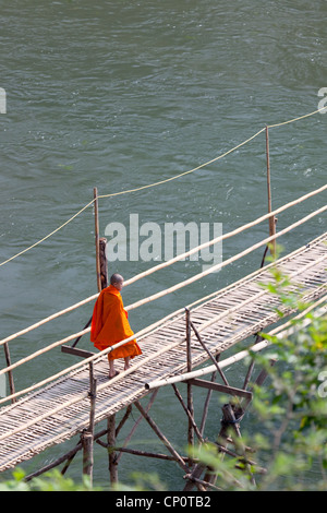 Ein Novize mit der fadenscheinigen Bambus Fußgängerbrücke über den Khan River, einem Nebenfluss des Mekong (Luang Prabang - Laos) geworfen. Stockfoto