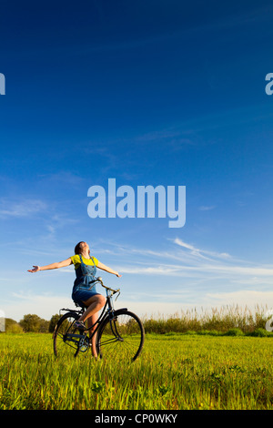 Glückliches Mädchen über ein Fahrrad und suchen Sie die Ansicht auf einer grünen Wiese Stockfoto