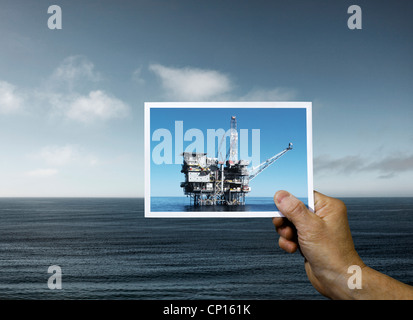 Hand mit Foto der Ölplattform Ozean Stockfoto