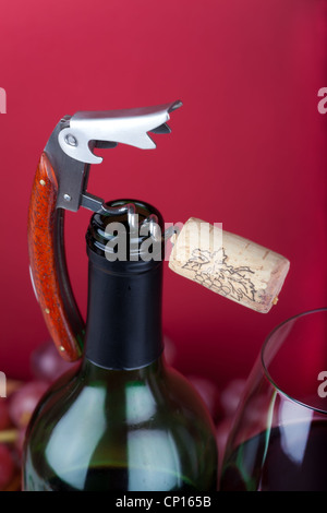 Korkenzieher mit Kork an der Oberseite Engpass neben einem Glas Rotwein Stockfoto