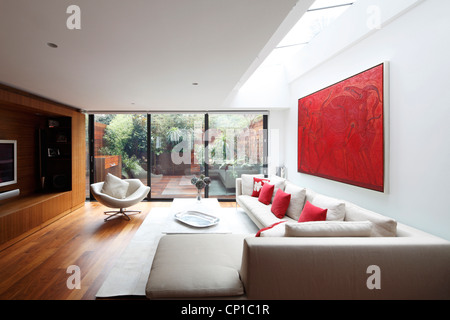 Wohnzimmer mit Lichtbrunnen über moderne Kunst und Schiebetüren zum Garten, London, UK. Stockfoto