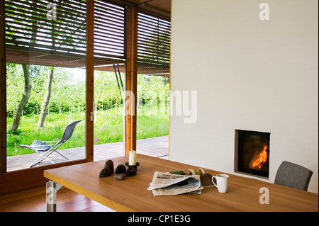 Holztisch vor brennenden Feuer in einfache Kamin im Zimmer Stockfoto