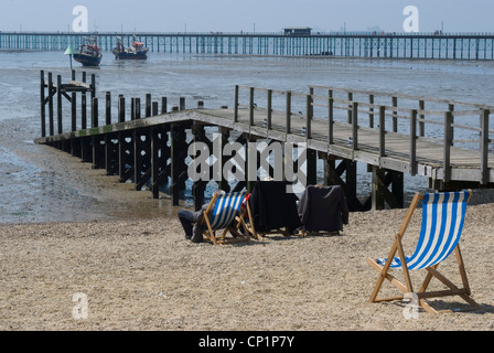 Liegestühle und Urlauber am Kiesstrand, bei Ebbe, mit Blick in Richtung Southend Pier Stockfoto