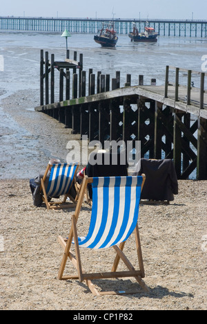 Liegestühle am Kiesstrand bei Ebbe, mit Blick in Richtung Southend Pier Stockfoto