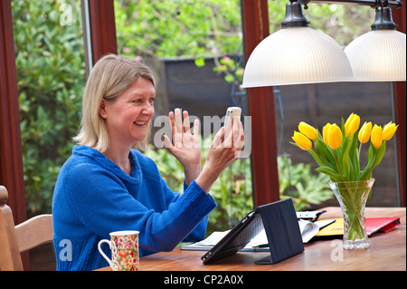 Blonde Frau zu Hause im Wintergarten mit ihrem iPad Tablet-Computer und mit video-Anruf auf ihrem Smartphone iPhone 4 s Stockfoto