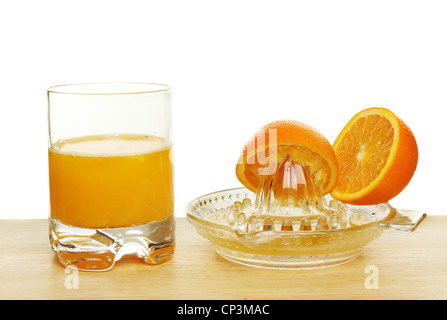 Frisch gepresster Orangensaft in ein Glas mit Fruchthälften und eine Saftpresse auf einem Holzbrett vor einem weißen Hintergrund Stockfoto