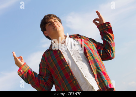 Yoga-Mann - junge Teenager mit erhobenen Armen Meditation Übungen. Lustige Sommer im Freien Schuss vor blauem Himmel. Stockfoto