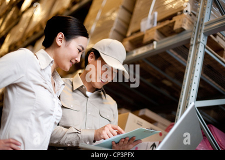 Chinesische Unternehmerin in einem Lager mit Arbeiter mit einem laptop Stockfoto