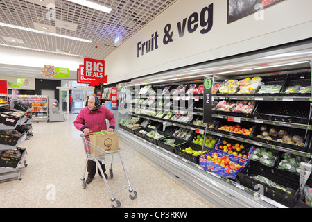 Alte Frau schob einen Wagen in einem Supermarkt einkaufen. Obst und Gemüse Gang. Stockfoto