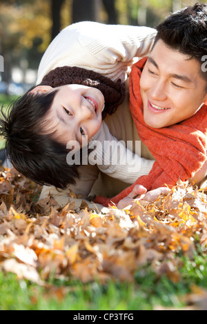 Vater und Sohn liegen auf dem Rasen umgeben von Autumn Leaves Spaß Stockfoto