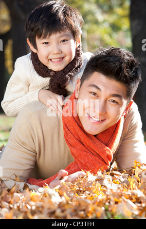 Vater und Sohn liegen auf dem Rasen umgeben von Autumn Leaves Spaß Stockfoto