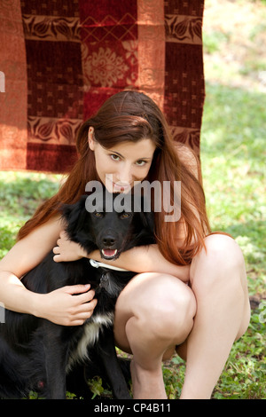 eine lächelnde Frau umarmt einen schwarzen Hund Stockfoto