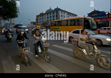 Motorräder, Fahrräder und Autos Fahrt entlang einer der wichtigsten Straßen in Hohhot mit Bewegung verwischen und Blitz in der Abenddämmerung zu füllen. Stockfoto