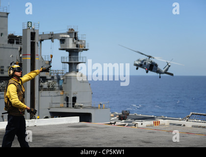 Aviation Boatswain's Mate (Handling) 2. Klasse Michael Edwards Signale an einen MH-60S Sea Hawk Hubschrauber zugeordnet Helicopter Sea Combat Squadron (HSC) 9 auf dem Flugdeck des Flugzeugträgers USS George H.W. Bush (CVN 77) während eines Kampfmittelübergangs mit dem Militärsealift Command Trockenfracht- und Munitionsschiff USNS Lewis und Clark (T-AKE 1). George H.W. Bush ist im Atlantischen Ozean und führt die Qualifikationen der Spediteur durch. Stockfoto