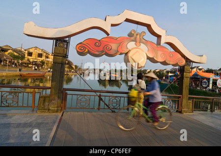 Horizontale Ansicht einer traditionell gekleidete alte Dame Radfahren auf dem Thu Bồn Fluss Klappbrücke Kreuzung im Zentrum von Hoi An, Vietnam. Stockfoto