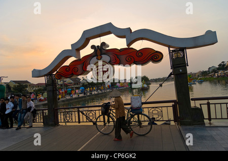 Horizontale Ansicht eine traditionell gekleidete alte Dame mit ihrem Fahrrad auf der Klappbrücke Thu Bồn Fluß in Hoi an ein bei Sonnenuntergang. Stockfoto