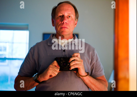 Porträt eines mittleren Alters männlichen Fotografen reflektiert in einem Spiegel Stockfoto