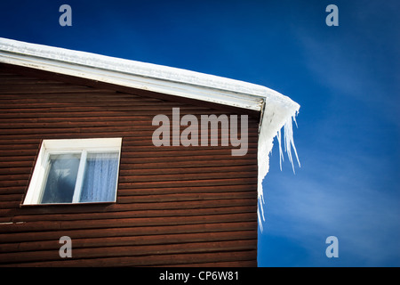 Winter/Berg-Konzept: Nahaufnahme von einem Holzhaus Dach bedeckt mit Schnee und Eiszapfen gegen blauen Himmel Stockfoto