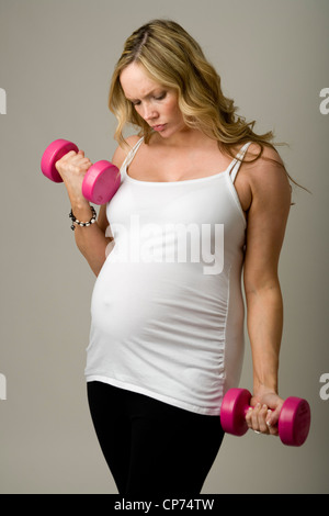Neun Monate schwangere Frau stehend Gewichte halten in ihren Händen. Stockfoto