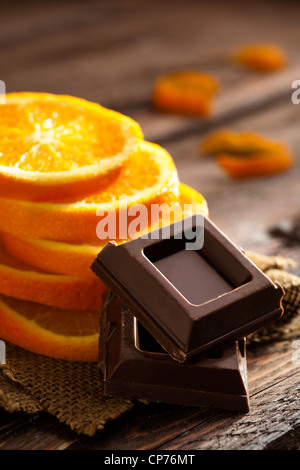 Schokolade-Quadrate mit Orangen Scheiben auf Jute und Holz Stockfoto