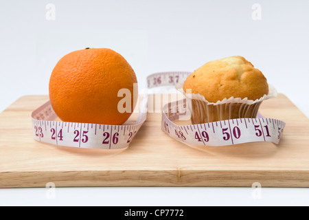 Orange und ein Muffin auf Schneidebrett mit Maßband Darstellung der höheren Zahl rund um den Muffin und unteren um orange Stockfoto