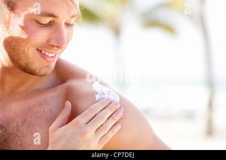 Glückliche junge kaukasischen Männermodel legte Bildschirm Sonnencreme Sonnencreme auf Schulter am Strand während der Sommerferien Stockfoto