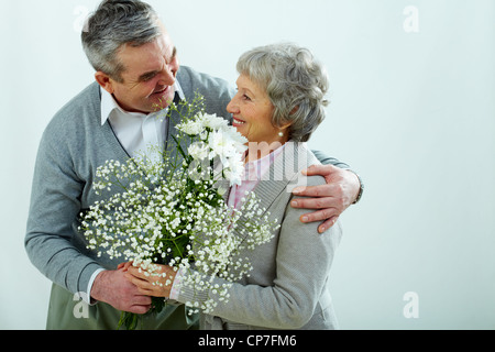 Reifer Mann präsentiert seine bessere Hälfte mit weißen Blüten, isoliert auf grau Stockfoto