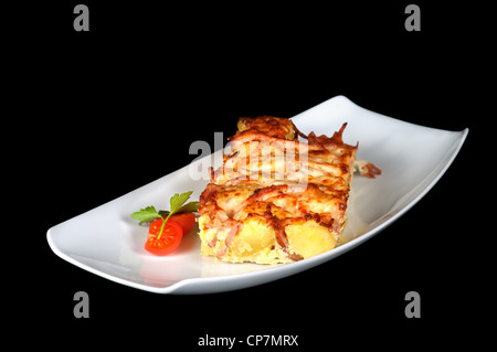 Bratkartoffeln mit Speck und Käse angeordnet mit Tomaten und Petersilie auf schwarzem Hintergrund isoliert Stockfoto