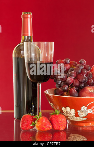 Rotwein Flasche und Rotwein im Glas mit roten Äpfeln, Trauben und Erdbeeren Stockfoto