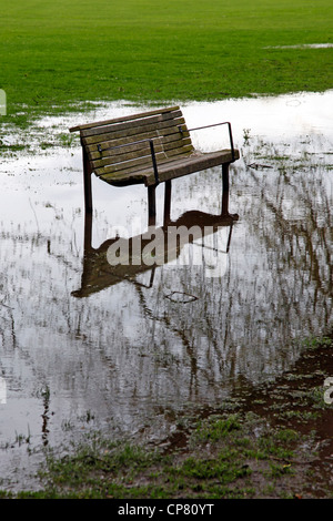 Leere Holzbank im überfluteten Park mit Reflexion der Baum im Wasser in Cambridge, England Stockfoto