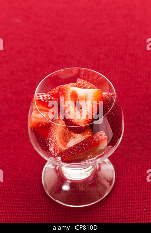 Glasschale mit frisch geschnittenen Erdbeeren Früchte gegen einen roten Tischdecke Stockfoto