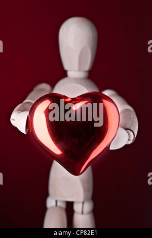 Eine Holzpuppe hält ein rotes Herz, als Symbol für Liebe. Stockfoto