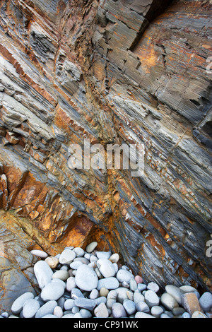 Nahaufnahme von bunten Gesteinsschichten mit einem Haufen von Kiesel am Fuße der Klippe, Sandymouth, Cornwall, UK Stockfoto