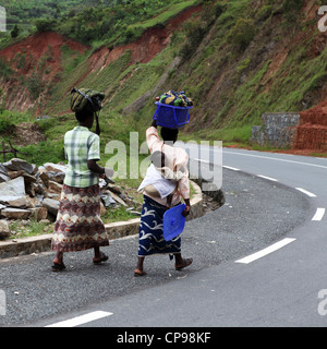 Frauen tragen waren auf den Kopf und man trägt ein Baby auf dem Rücken im ländlichen Ruanda. Die Frauen gehen an einem Straßenrand. Stockfoto