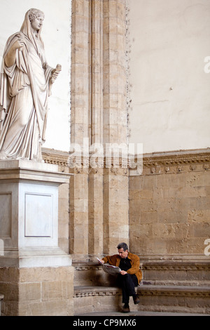 Mann liest eine Zeitung an der Loggia dei Lanzi. Die Statue der Sabinerinnen, aus der Zeit des Trajan - Hadrian in der Römerzeit. Stockfoto