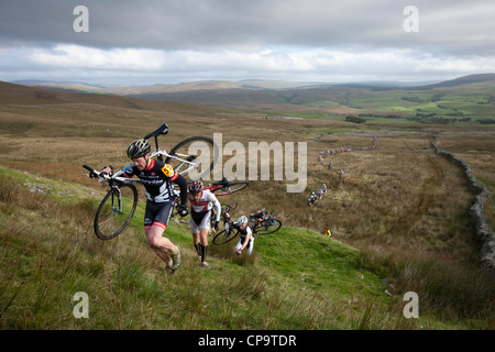 Radfahrer tragen ihre Fahrräder auf einem steilen Hügel während drei Gipfeln Cyclo-Cross in North Yorkshire, England, Vereinigtes Königreich Stockfoto