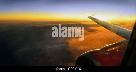 Jet Flugzeugflügel fliegen hoch über schöne Wolkengebilde Berge bei Sonnenuntergang. Stockfoto