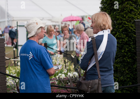 Die Menschen/-Garten für Krebsforschung Großbritannien als weibliche Freiwillige steht im Gespräch mit Designer-RHS Flower Show, Tatton Park, Cheshire, England. Stockfoto