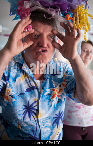 Ein älterer Mann macht ein lustiges Gesicht beim Tragen einer bunte Mütze.  Eine glückliche junge Frau blickt auf.  Ein buntes Hemd tragen. Stockfoto