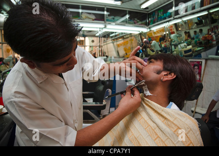 Junge arabische Mann aus Dubai bekommen eine Nassrasur mit einem offenen Rasierer in einem traditionellen Friseure-Shop. Altstadt-Souk. Stockfoto