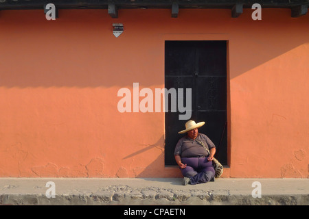 Guatemala Antigua Mann mit Sombrero-Hut sitzt durch bunte Wand cobble stone Straßenszene der UNESCO Stockfoto